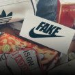 Des produits de mode (sacs, chaussures) dont les logos parodient de fausses marques posés en vrac. On voit notamment un logo NIKE surmonté de la mention FAKE.