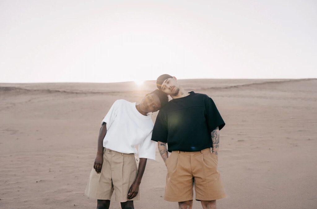 Deux mannequins, un homme et une femme, posent au milieu des dunes dans le desert. Ils portent u t-shirt et un short de la marque Flow Studio.