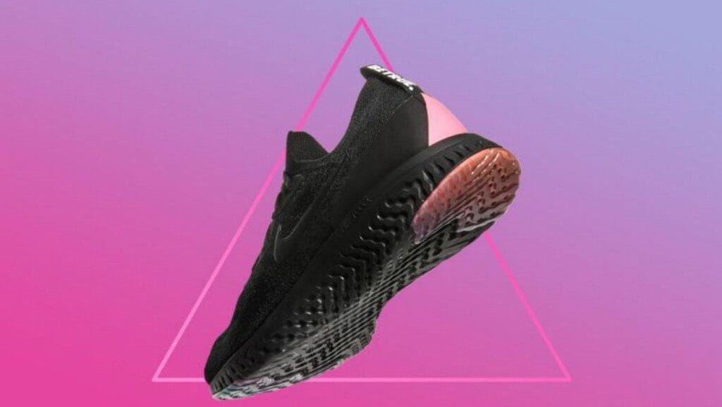 Une basket de la collection Pride 2018 de Nike. La basket est noire avec un triangle rose à l'arrière. Elle est photographiée sur fond de triangle rose et violet.