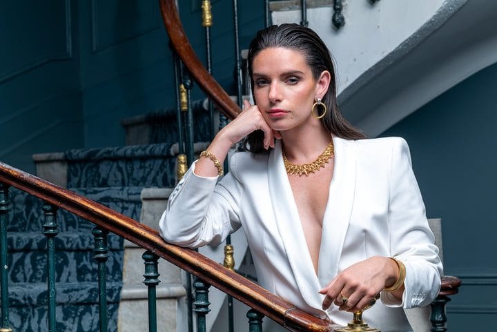 Une mannequin pose en blazer blanc avec des bijoux en or de chez Rivluxe Paris