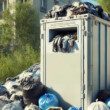 a container that usually in France receive used clothes. It's in the center of the image in a hyperrealistic type and 1920 x 700 px. In front, there is many bags piled up, themselves containing used clothes