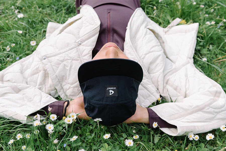 personne-allongée-dans-lherbe-avec-une-casquette-artefact